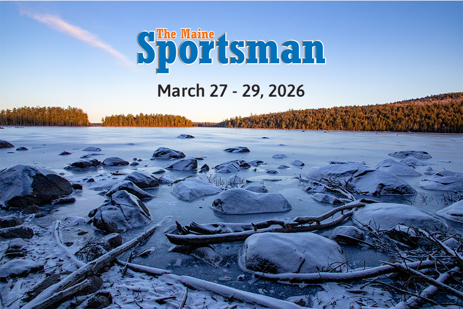 Snow-covered rocks and logs along a frozen lake shore under a clear sky, with text “The Maine Sportsman, March 27-29, 2026” overlaid at the top.